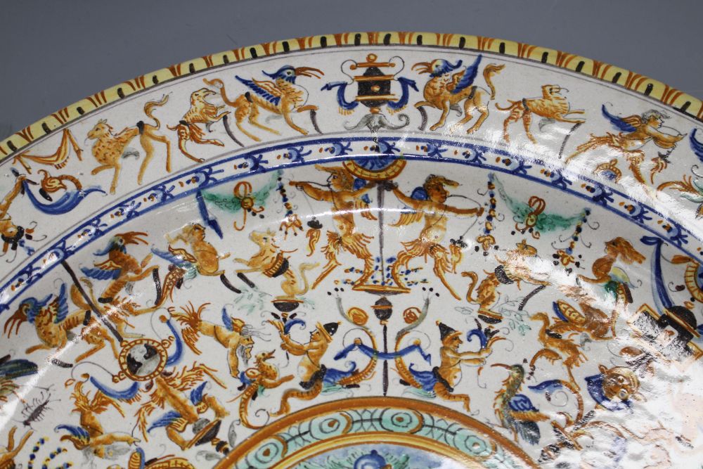 A 19th century Italian 17th century style maiolica charger, decorated with cherubs flanking a cartouche within bands of stylised beasts